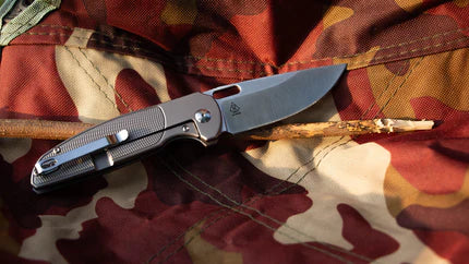 A folding knife with gray metallic handle lies on camouflage fabric background.