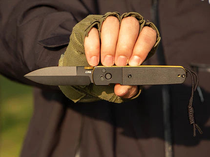 A gloved hand holding a black folding tactical knife in an open position.